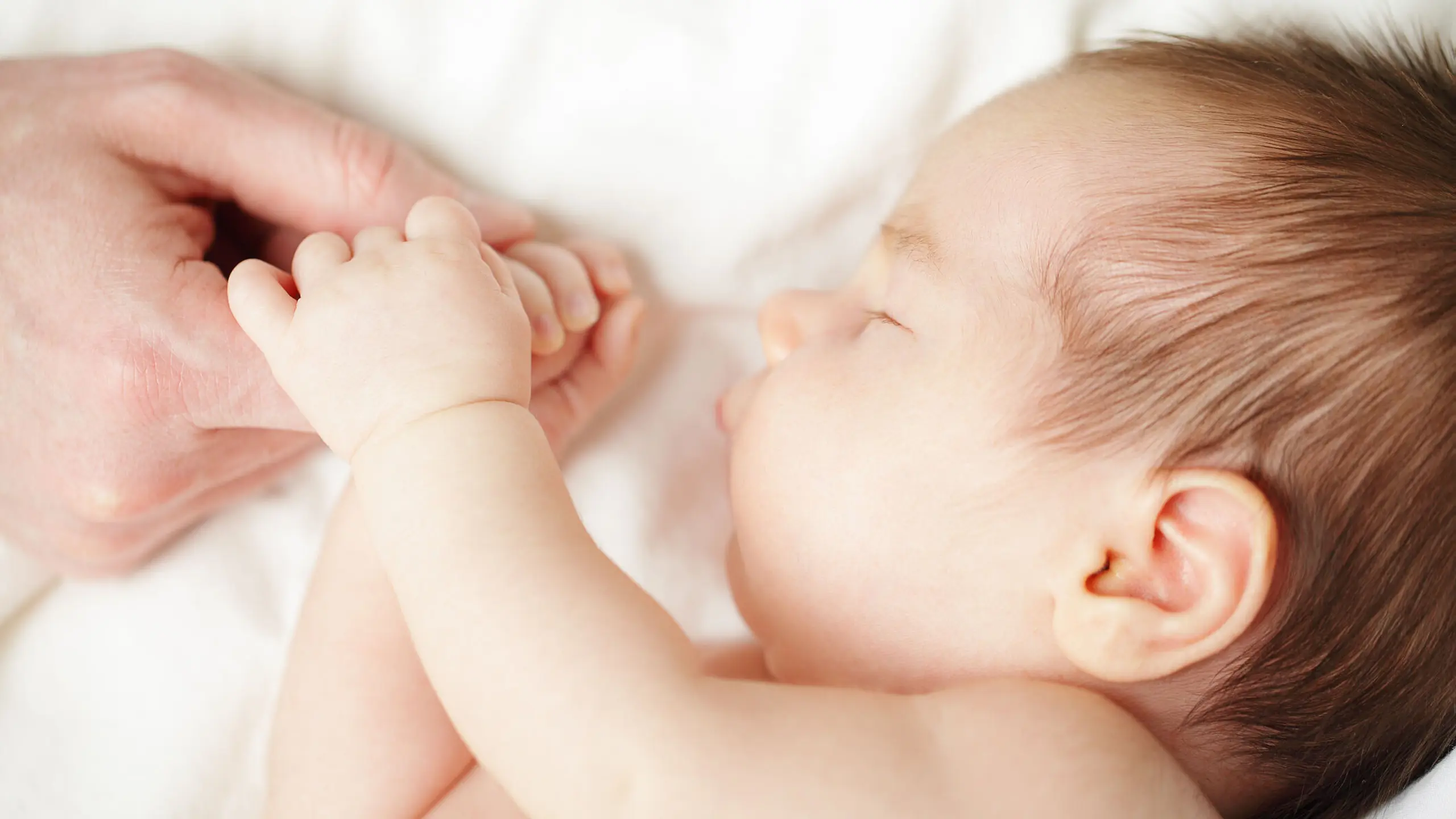 Baby, das schläft und dabei die Hand seiner Mutter hält