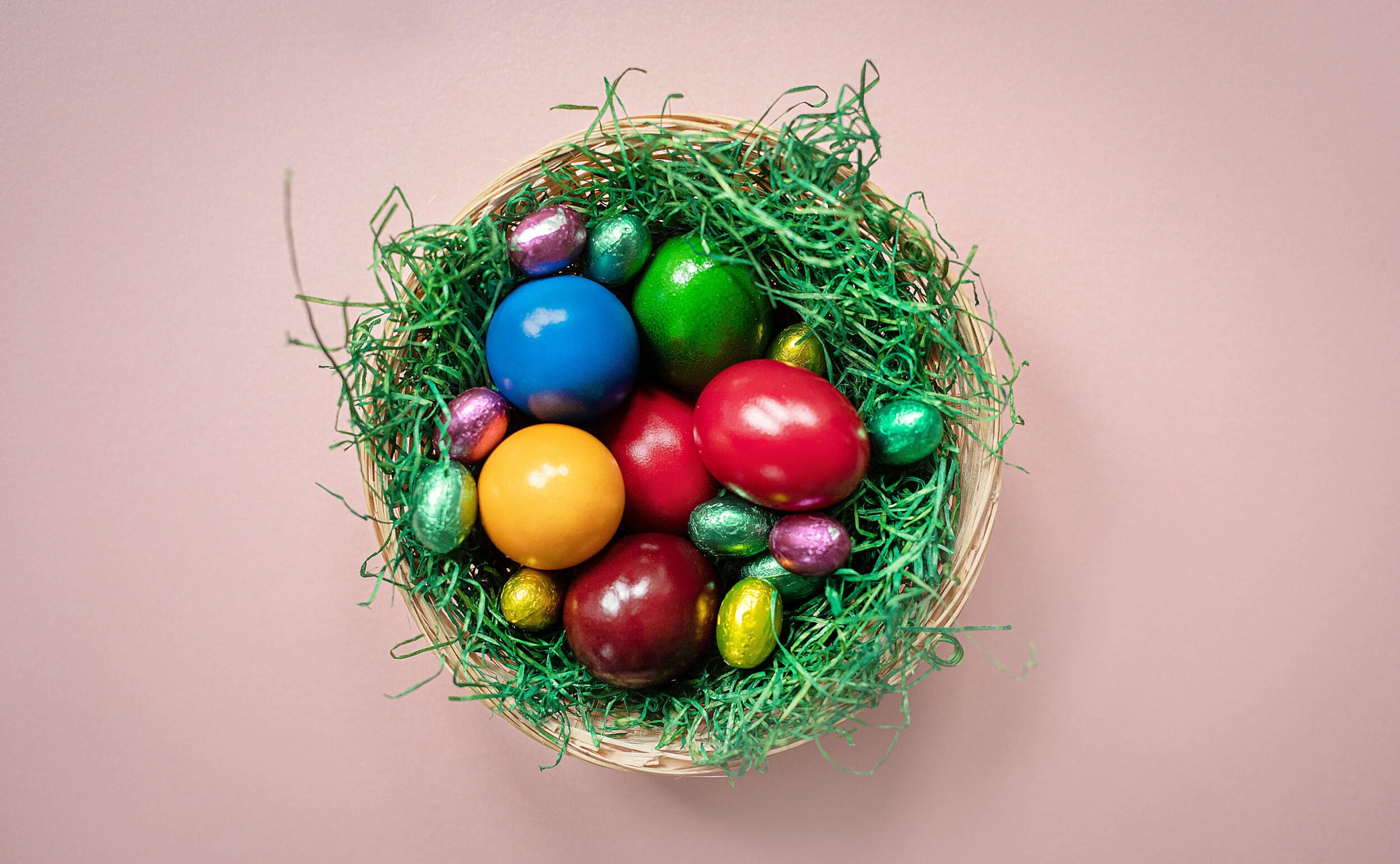 Osternest mit bunten Ostereiern, das auf einem rosa Hintergrund steht