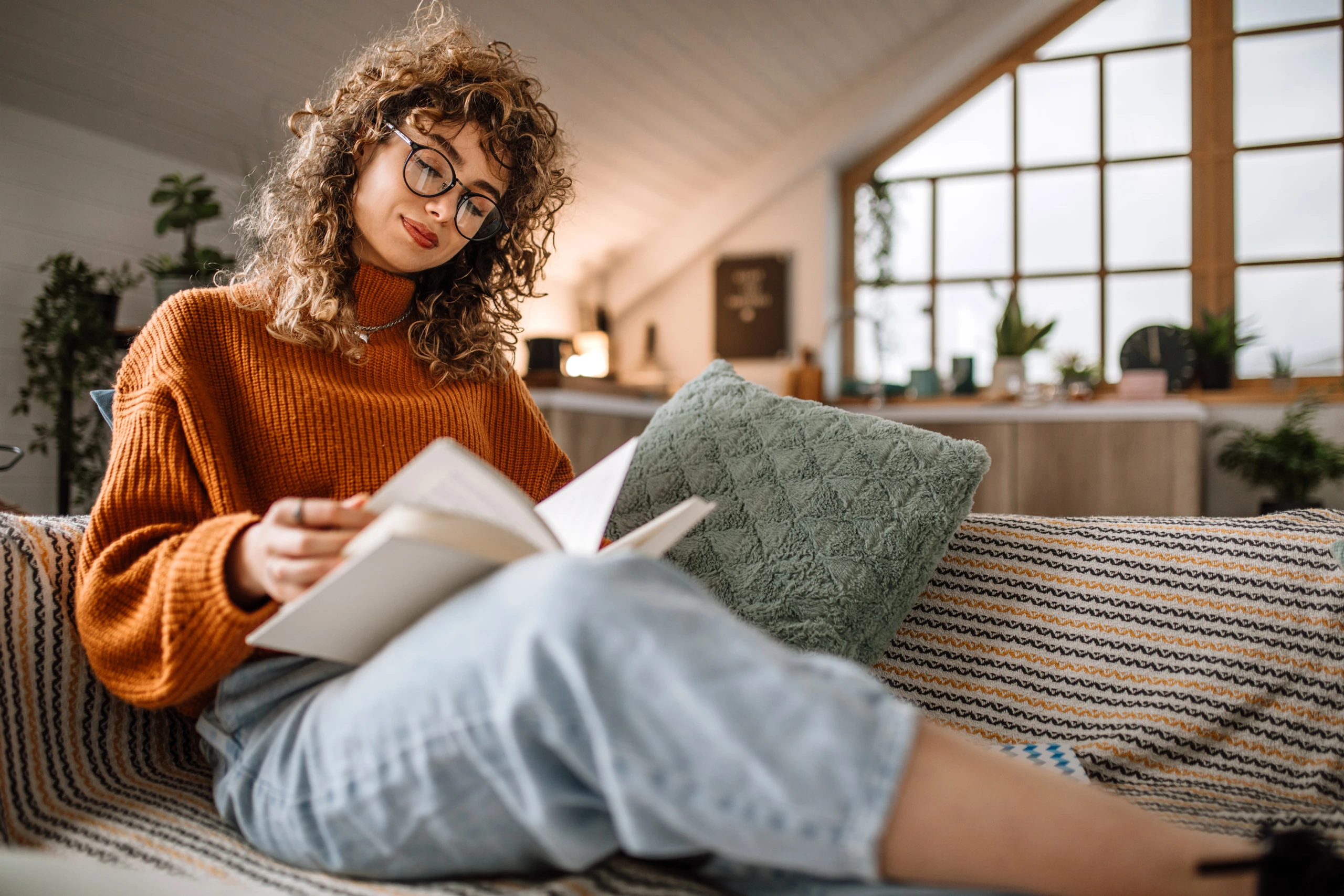 Frau, die auf einer kuscheligen Couch sitzt und ein Buch liest