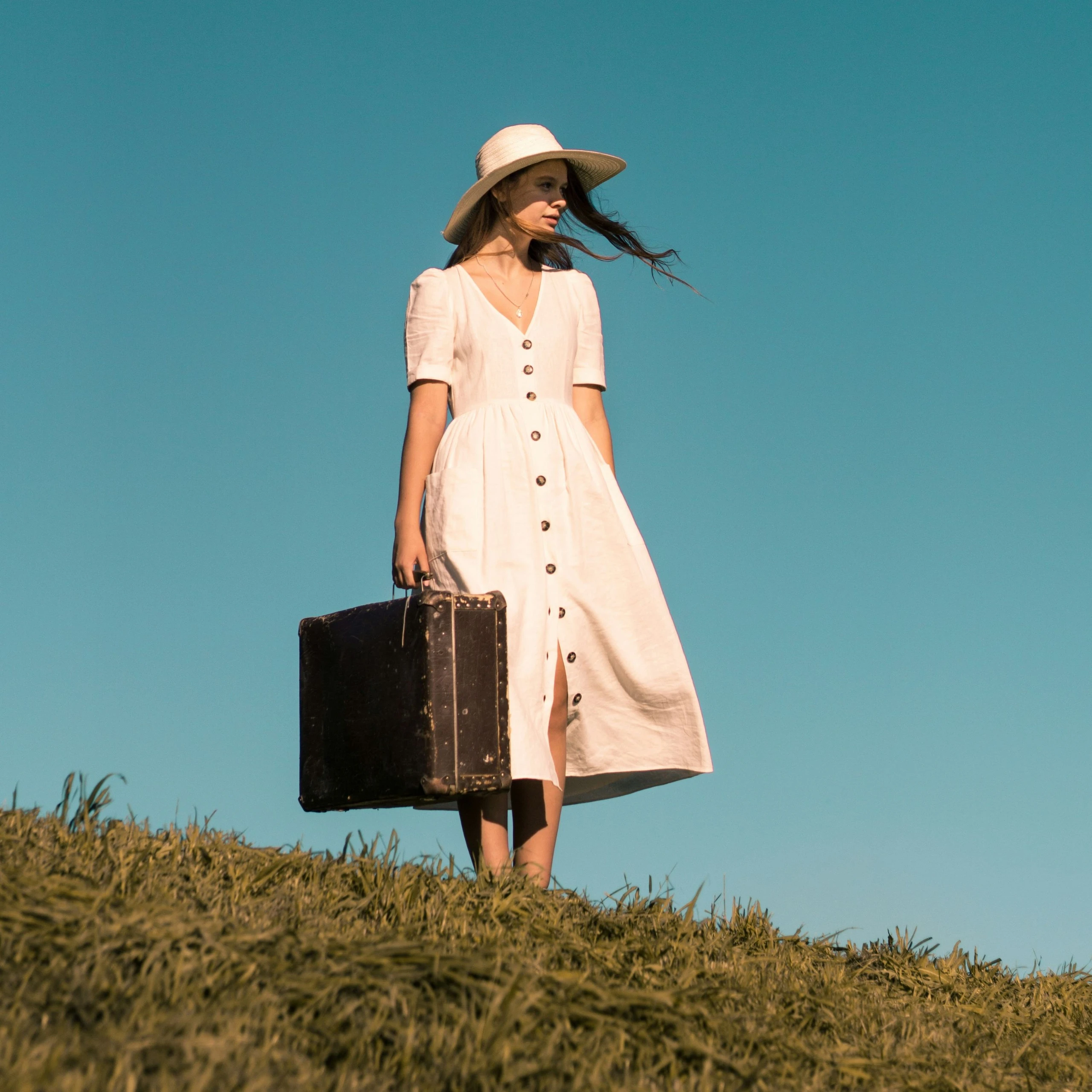 Frau steht mit Koffer in der Hand auf Wiese