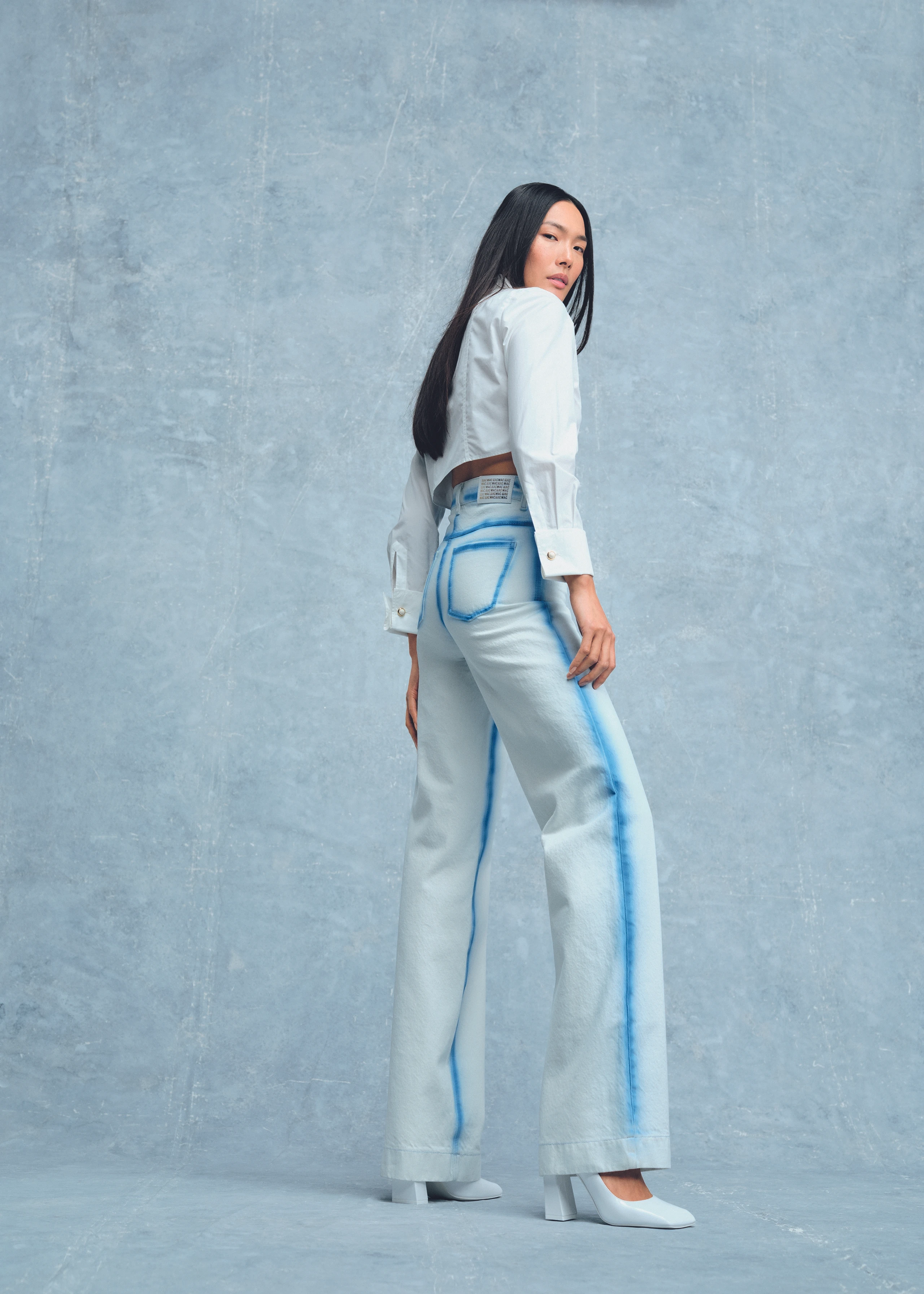 Model vor blauem Hintergrund mit Jeans und weißer Bluse