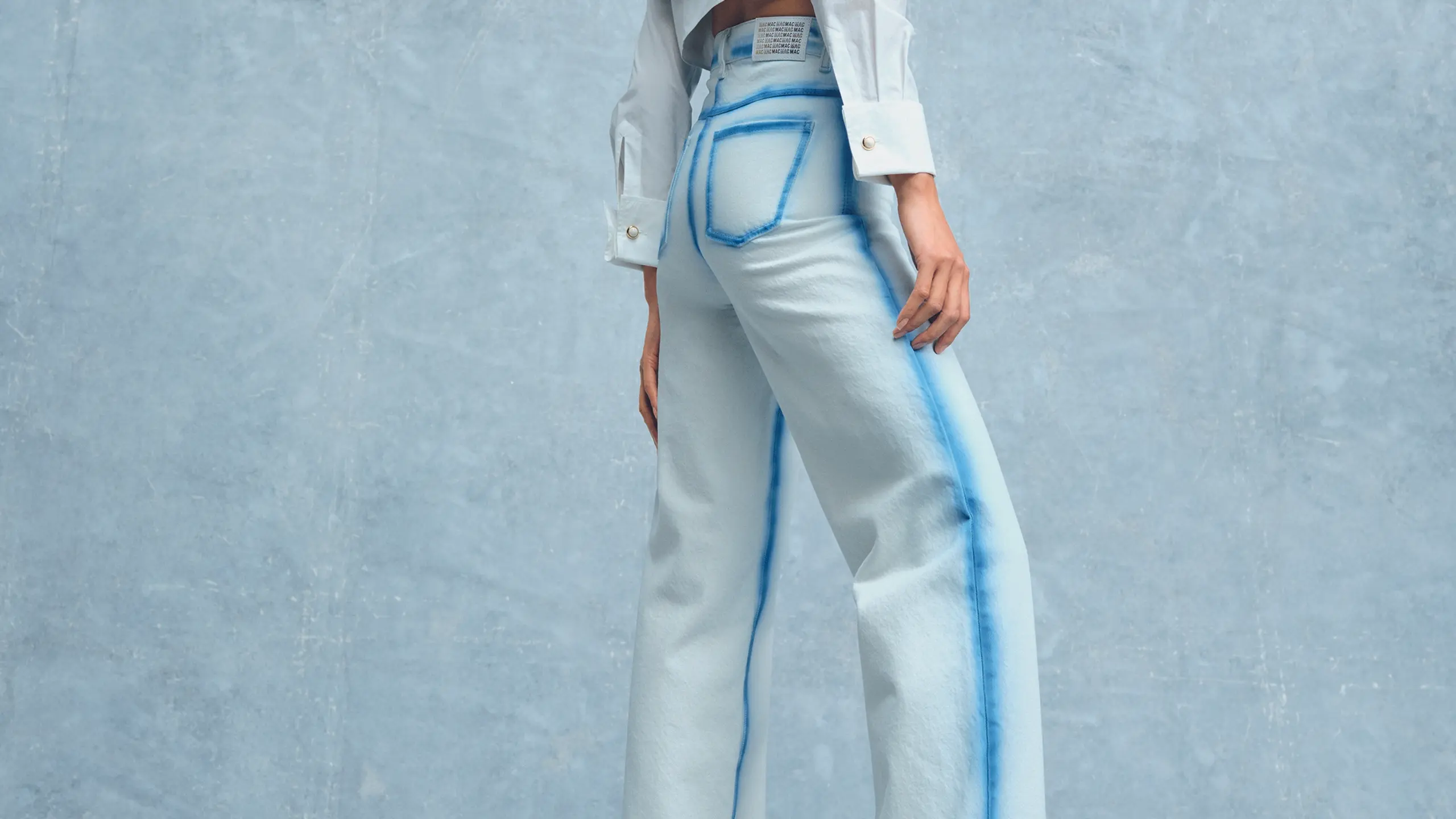 Model vor blauem Hintergrund mit Jeans und weißer Bluse