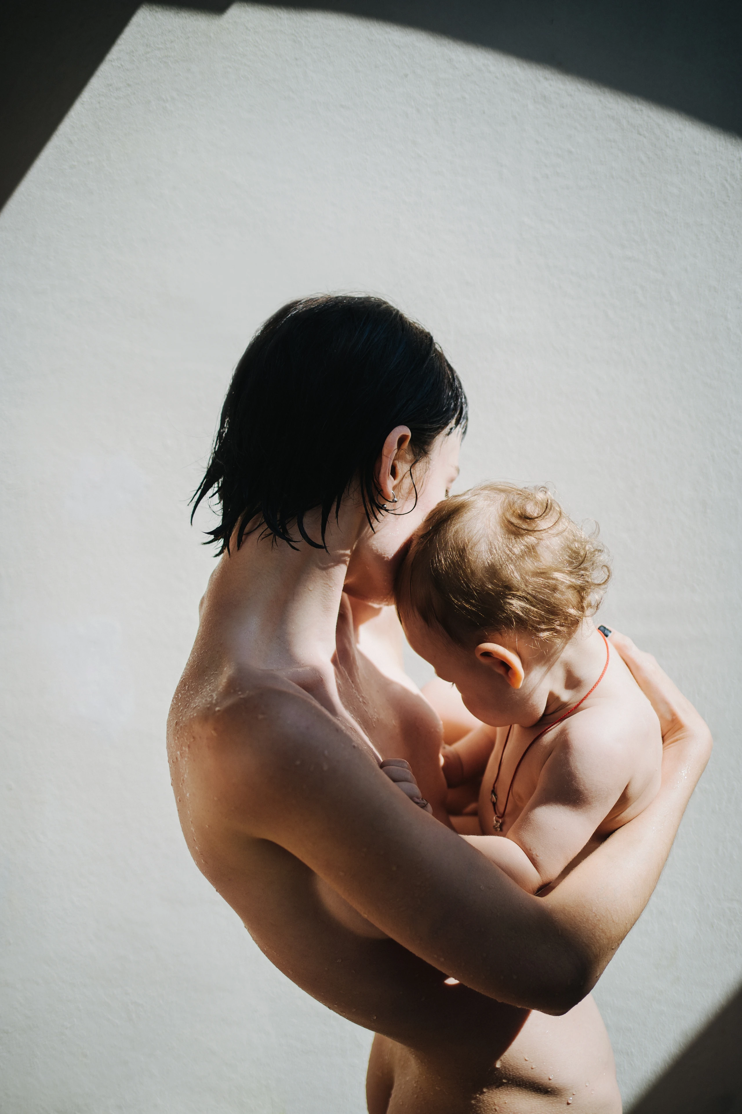 Eine nackte Frau hält ein nacktes Baby auf dem Arm, beide Gesichter schauen von der Kamera weg