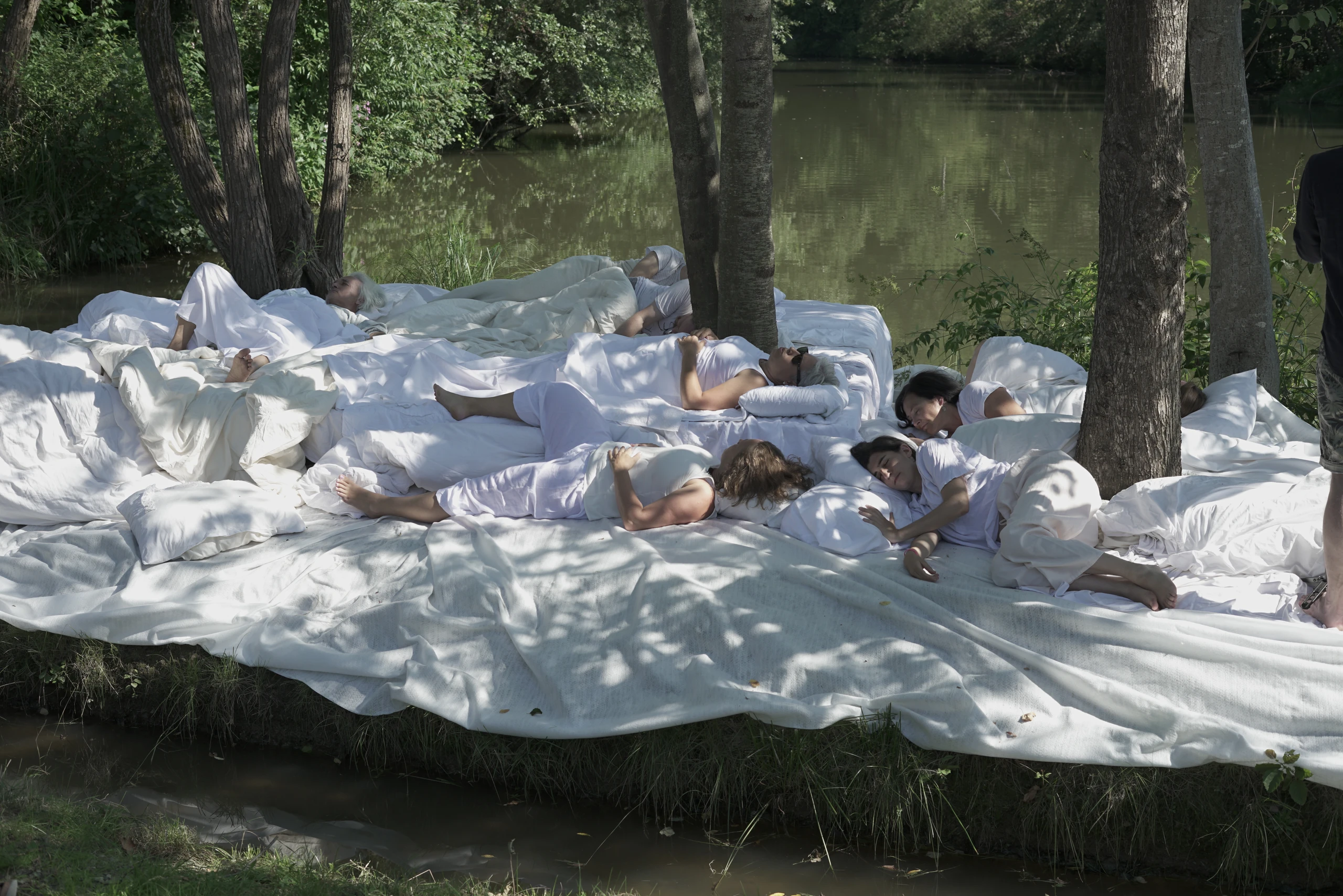 Szene an einem Fluss, Menschen liegen auf weißen Tüchern und Pölstern