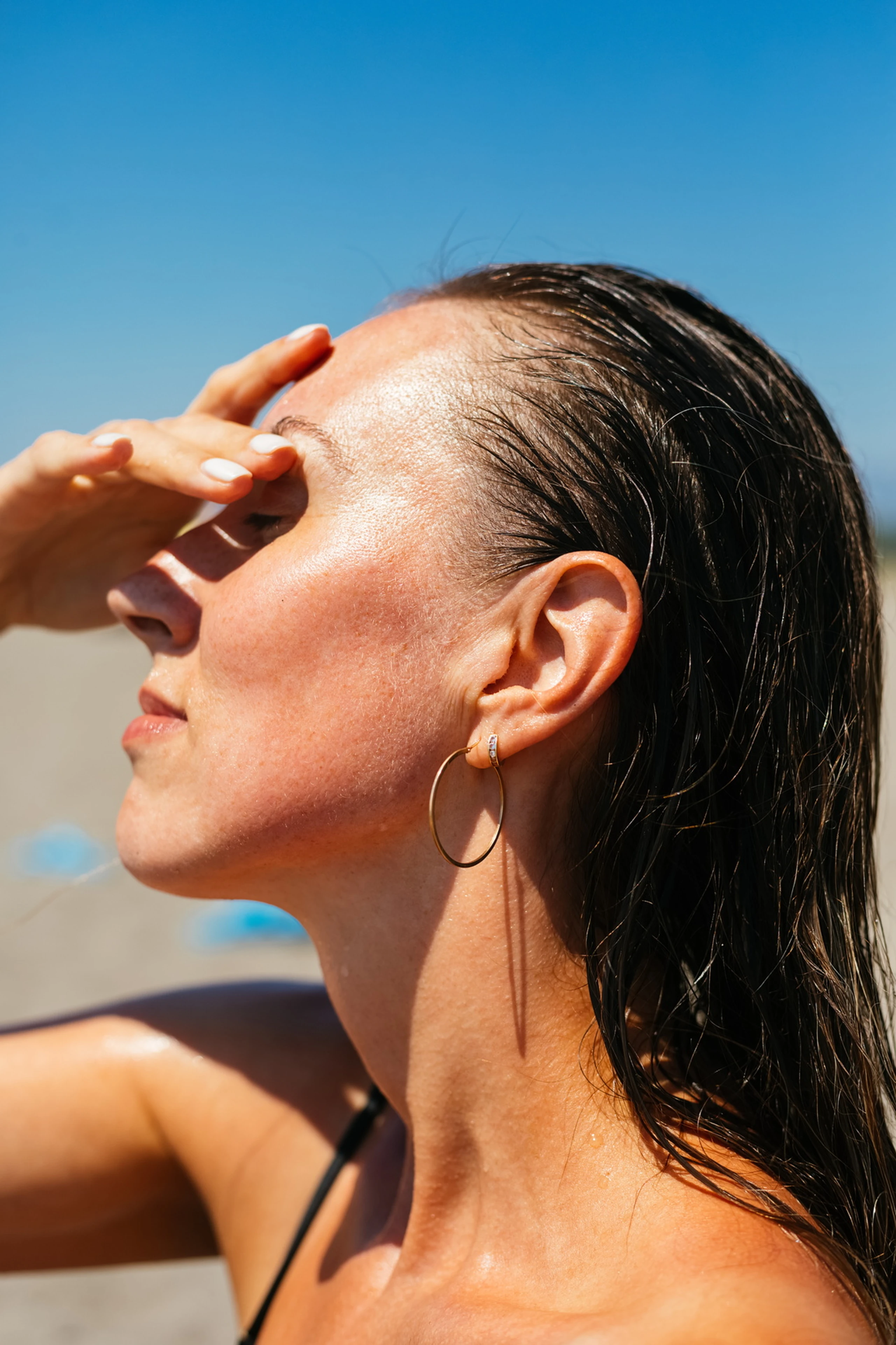 Frau mit nassen Haaren steht Richtung Sonne und bedeckt Augen