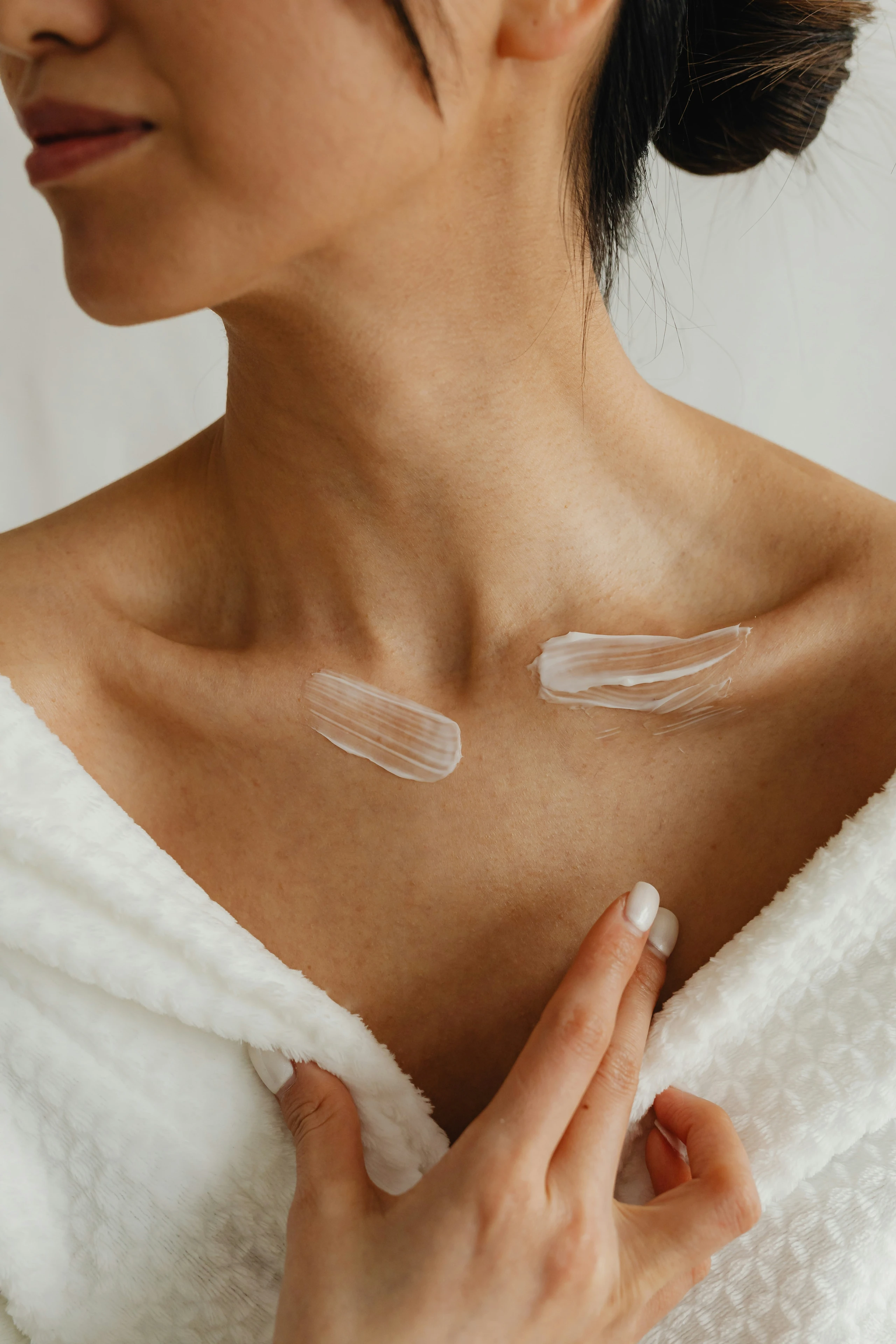 Frau in Bademantel mit Creme-Swatches auf den Schlüsselbeinen