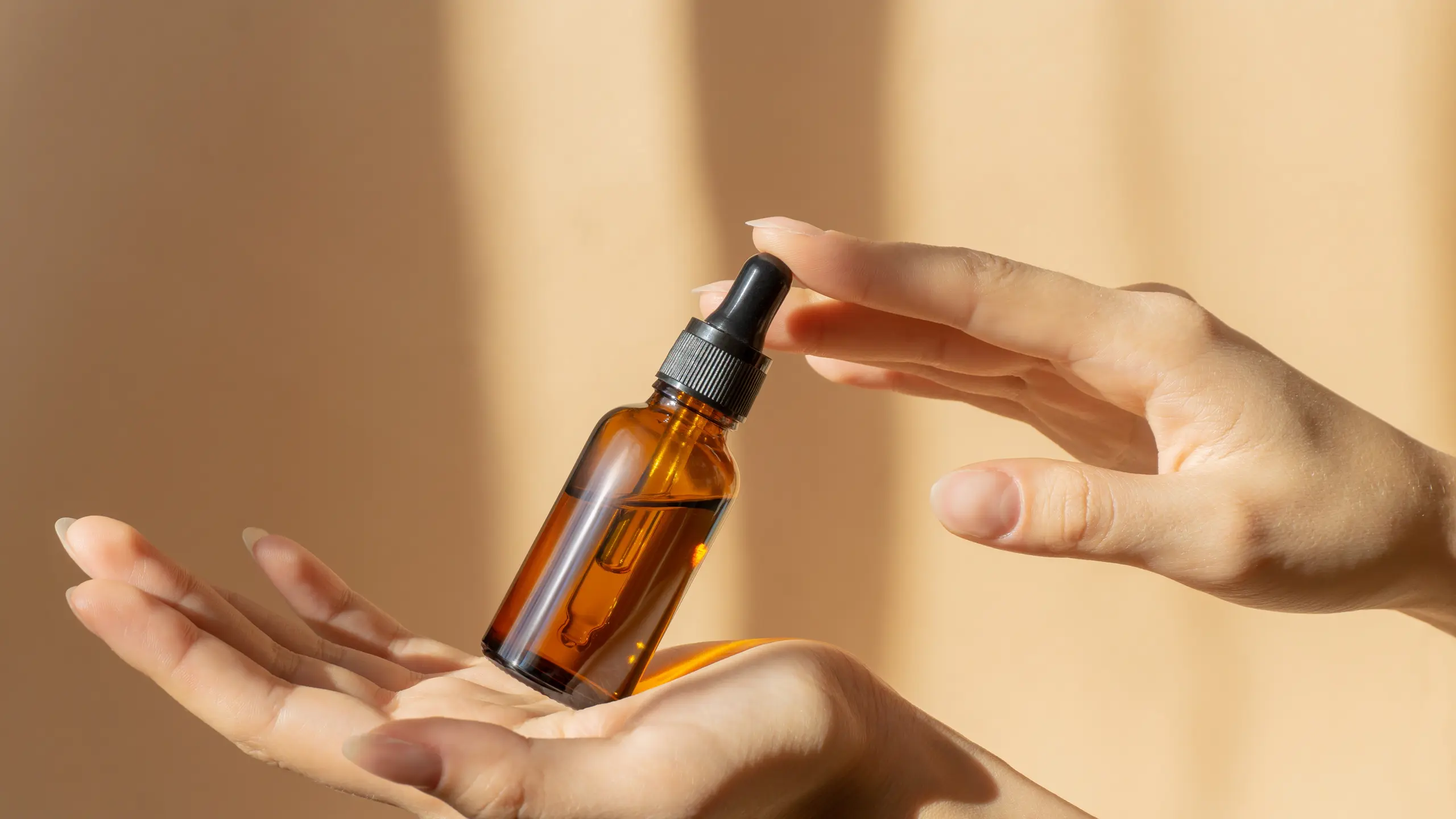 Zwei Hände halten ein geschlossenes Serum vor beigem Hintergrund